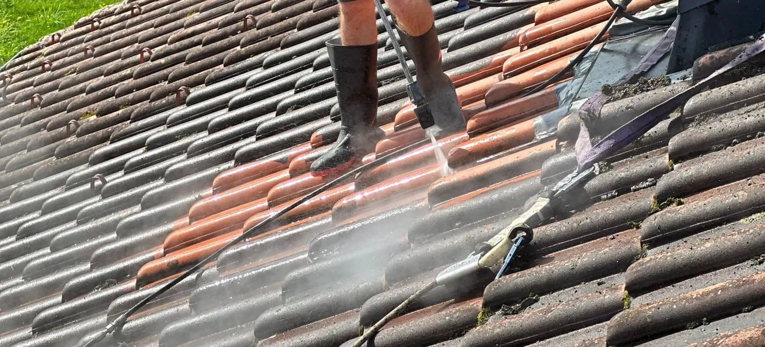 Nahaufnahme während der Reinigung, links die dunkel bemoosten Ziegel, rechts daneben die bereits gereinigten in ihrem ursprünglichen Rot, dazwischen der Wasserstrahl